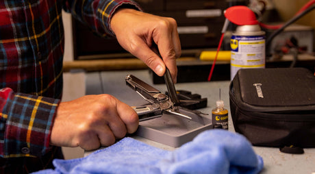 Translation missing: es.Person cleaning a stainless steel Leatherman Wave® Plus multitool on a workbench using the Leatherman Maintenance Kit