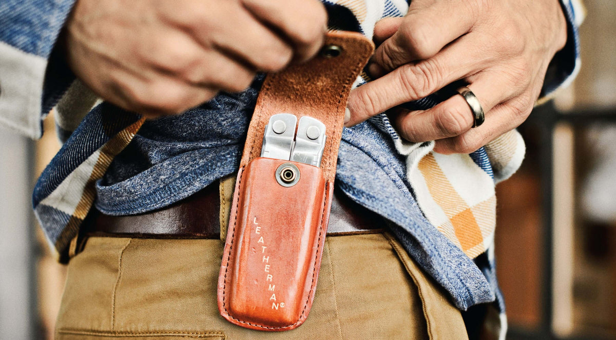 Person showcasing a brown Leatherman Heritage sheath on the side of a belt with a tool inside.