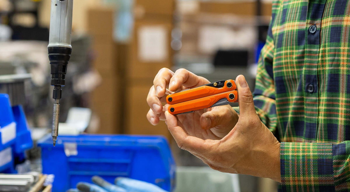 Jackson Wang holding an orange Leatherman Wave® Alpha multitool in a workshop setting.