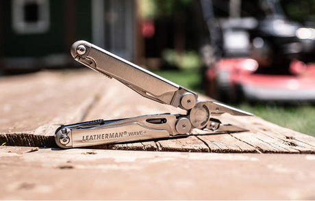 Translation missing: en.Stainless Steel Leatherman Wave+ multi-tool resting on a wooden surface outdoors, showcasing its sleek design and functionality
