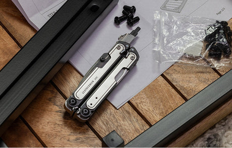 Translation missing: en.Leatherman Black DLC &amp; Stainless Steel ARC® on a wooden surface with the large bit driver extended, surrounded by screws and assembly instructions
