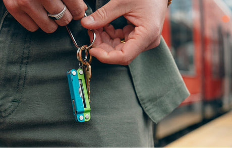 Translation missing: en.Person holding a Teal Twist Leatherman Micra® and keys while waiting at a train station, showcasing everyday carry essentials
