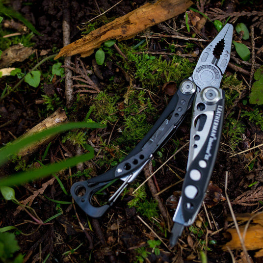 Translation missing: en.Black &amp; Stainless Skeletool® CX multitool resting on mossy forest floor, showing its sleek design and versatility