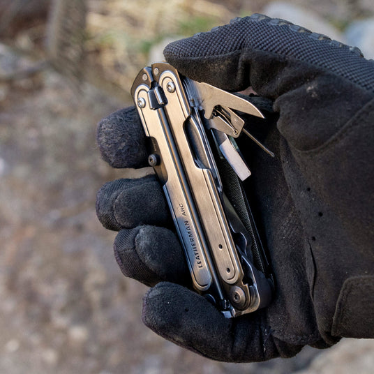 Translation missing: en.Black DLC &amp; Stainless Steel Leatherman ARC® held in a gloved hand, showcasing some tool included tools