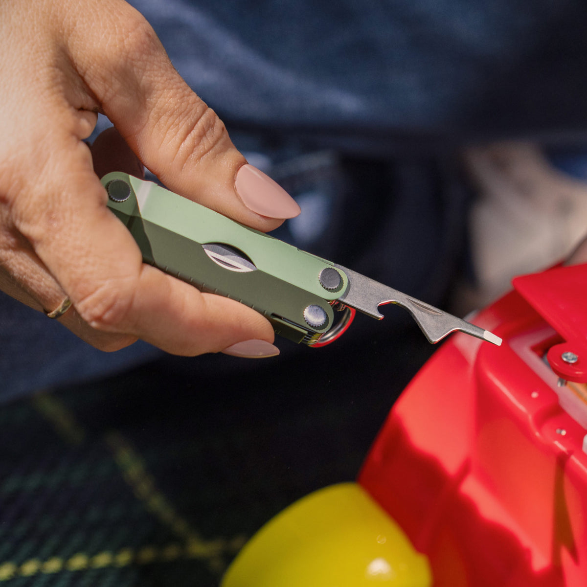 Translation missing: en.Hand holding a Cardamom Micra® multi-tool, using the extra-small screwdriver on a red plastic object