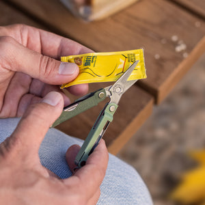 Translation missing: en.Hand using a Cardamom Micra® multitool scissors to cut open a small yellow packet
