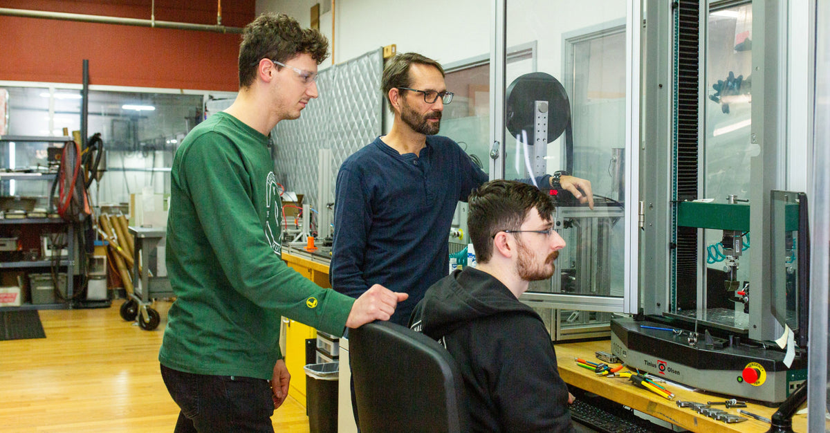 Translation missing: en.three men collaborating on a machine in a factory setting, focused on their task and surrounded by industrial equipment