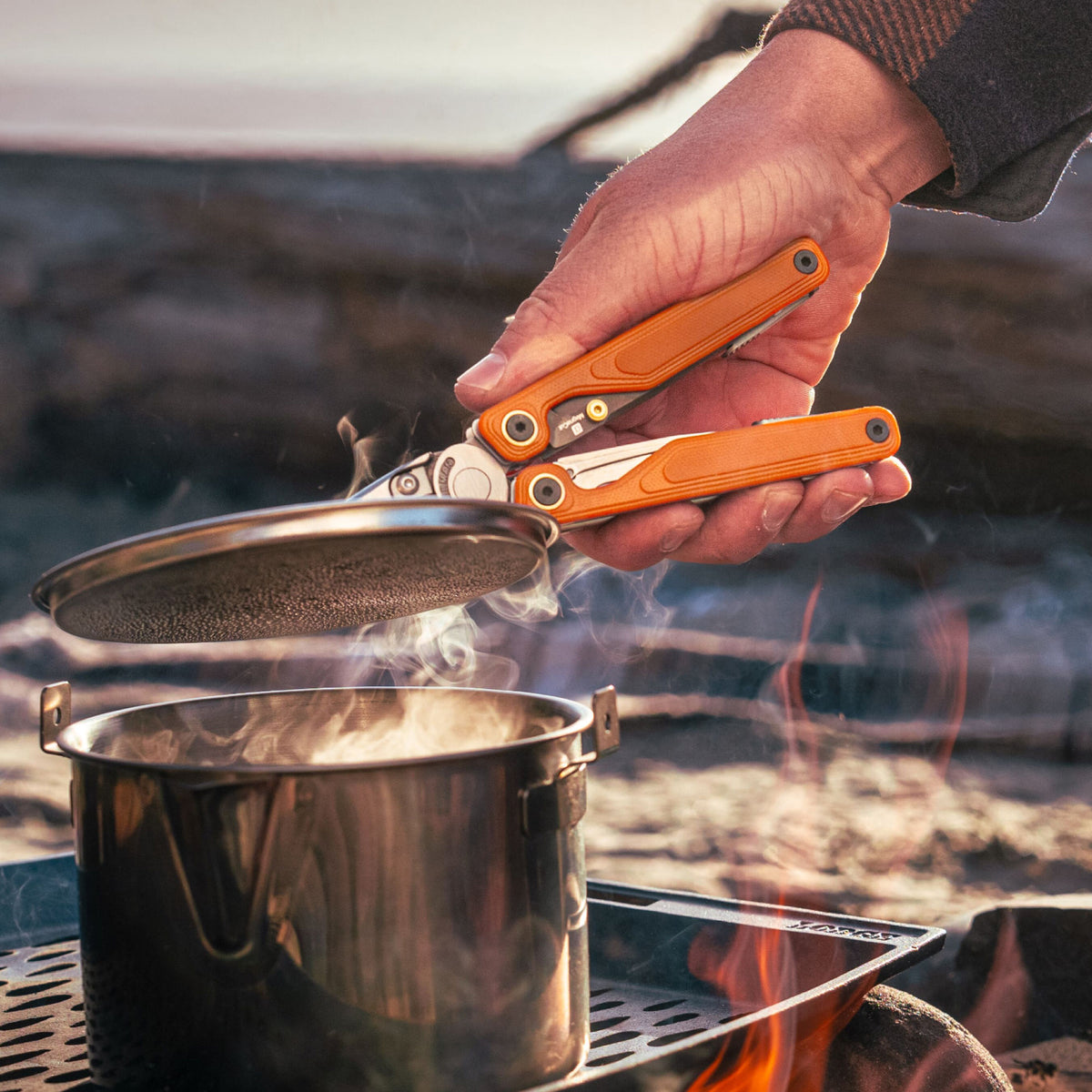 Translation missing: en.Person using Canyonland Leatherman Wave® Alpha multitool to remove a lid from a pot while camping outdoors