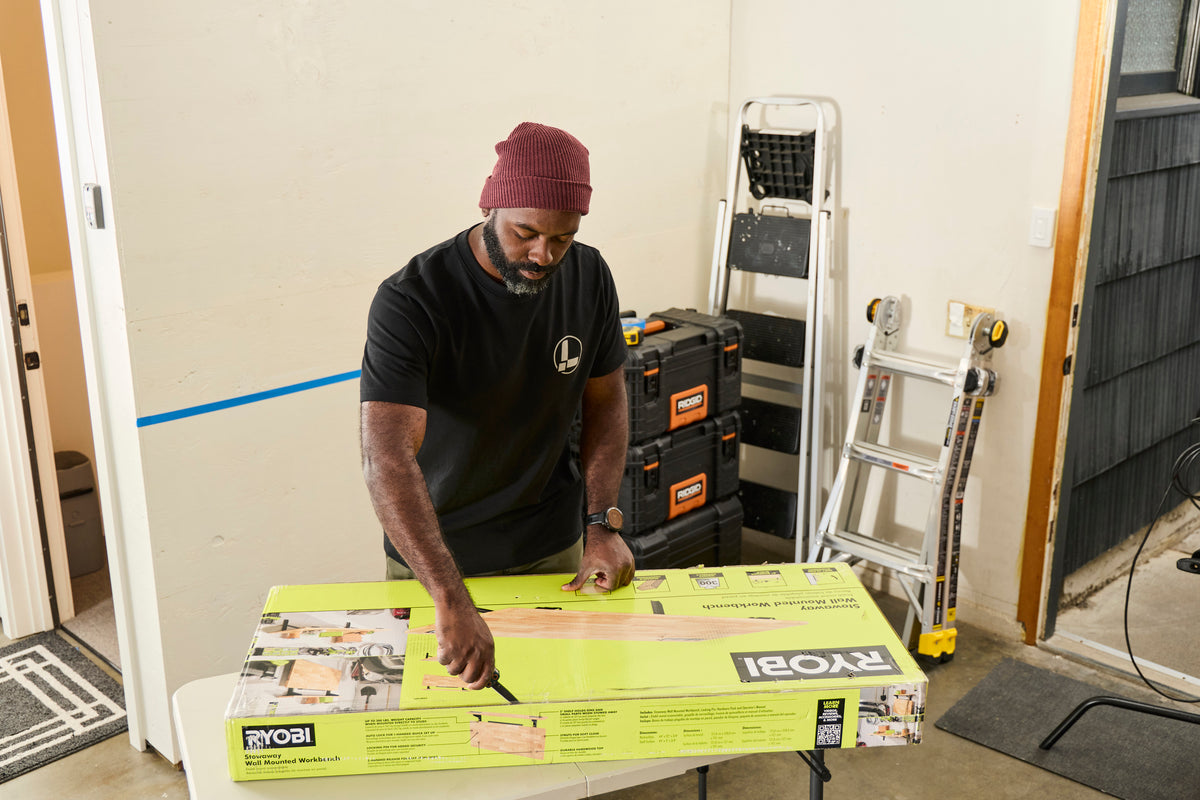 Translation missing: en.A person wearing a black Leatherman Classic Tee using the blade on a Leatherman multi-tool to open a large box that is laying on top of a folding table