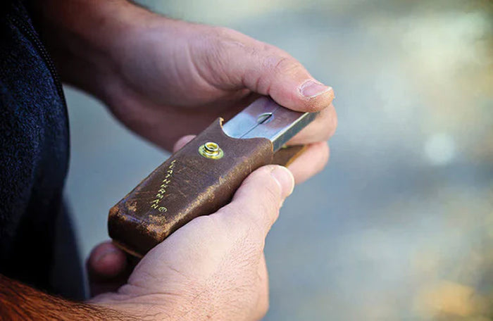 Translation missing: en.Person holding a brown leather Leatherman sheath with a multitool visible, showcasing its craftsmanship and design