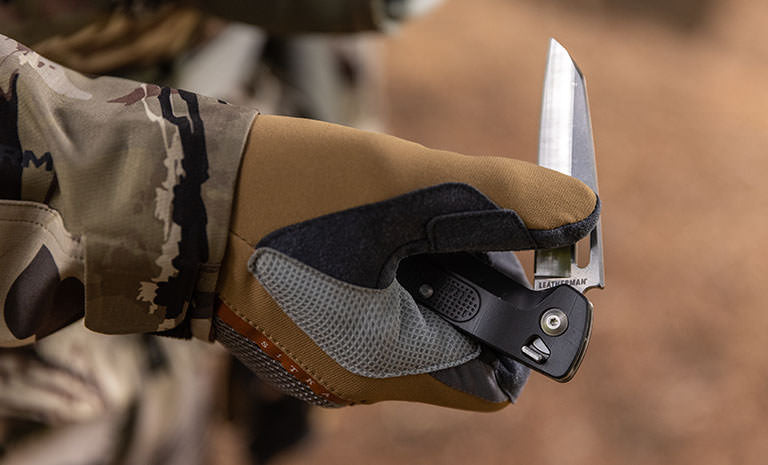 Translation missing: en.Man wearing camo jacking and tan brown leather gloves opening a Leatherman K4