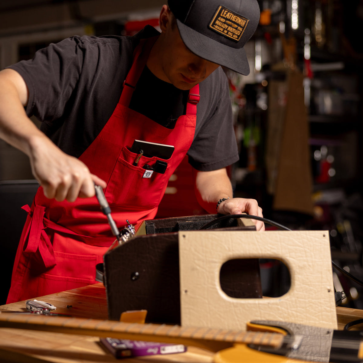 Translation missing: es.Person wearing a red apron repairing electronic equipment at a workbench in a garage workshop