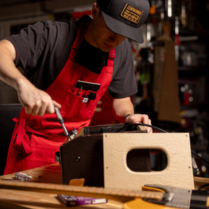 Translation missing: es.Person wearing a red apron repairing electronic equipment at a workbench in a garage workshop