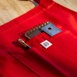 Translation missing: es.Red apron front pocket holding a pencil, small notebook, and metal ruler