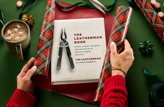 Translation missing: en.Person wrapping 'The Leatherman Book' with festive decorations, and a cup of hot cocoa