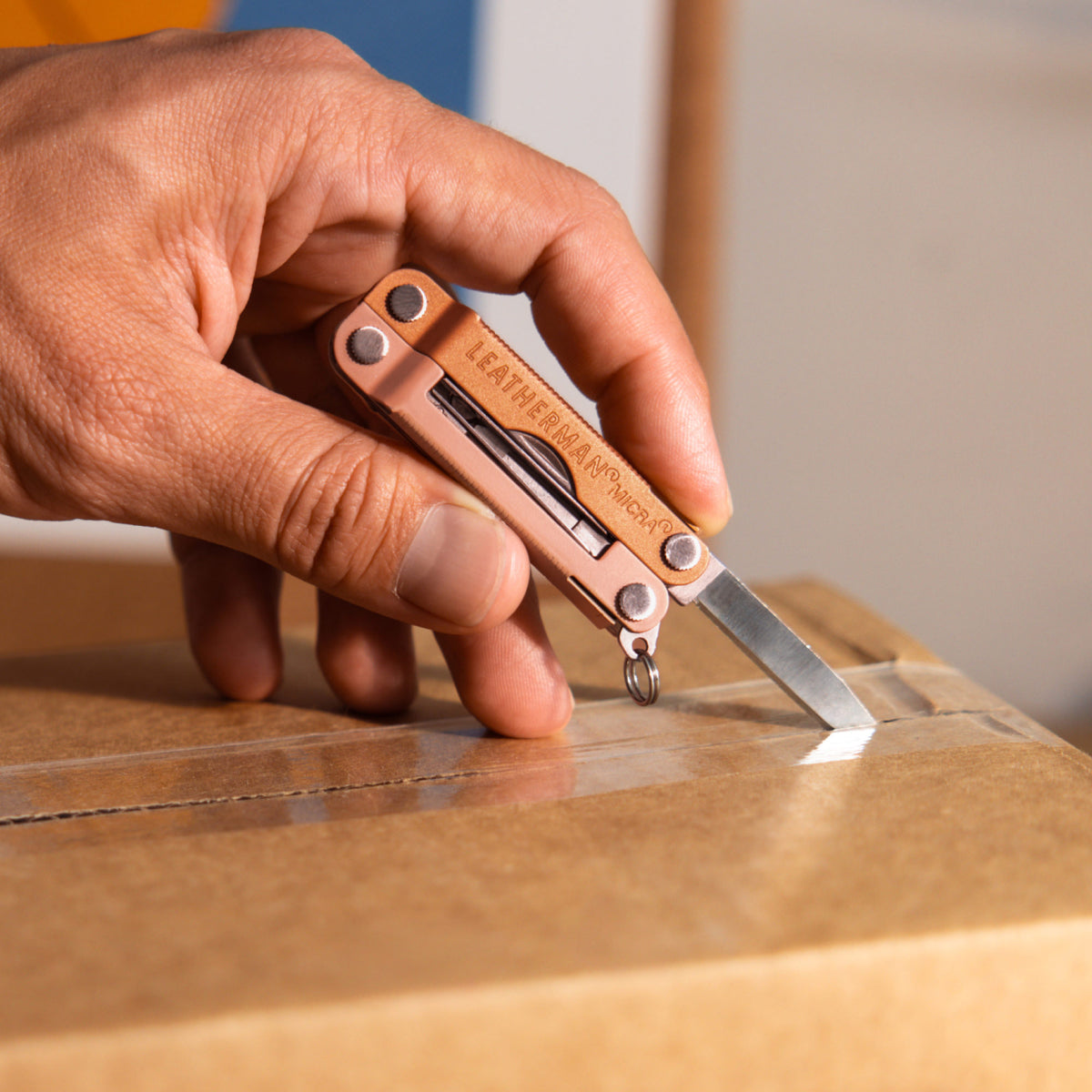 Translation missing: en.Hand using a Ginger Peach Micra® multitool knife blade to cut tape on a cardboard box