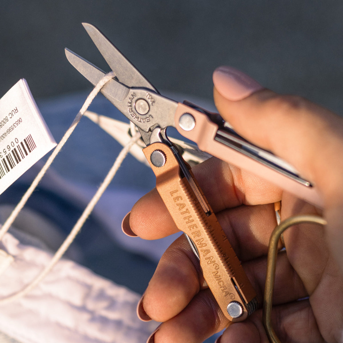 Translation missing: en.Hand using the scissors on a Ginger Peach Micra® to cut a string attached to a clothing tag
