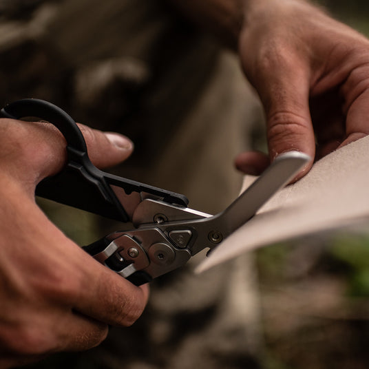 Translation missing: en.Close-up of hands using the scissors on a black Raptor Rescue to cut paper, showcasing focus and precision
