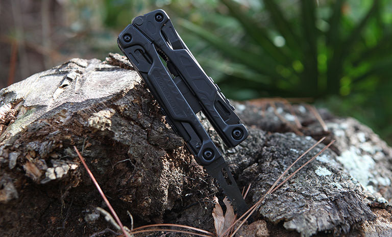 Translation missing: en.Black Leatherman OHT saw blade inside a piece of wood outdoors