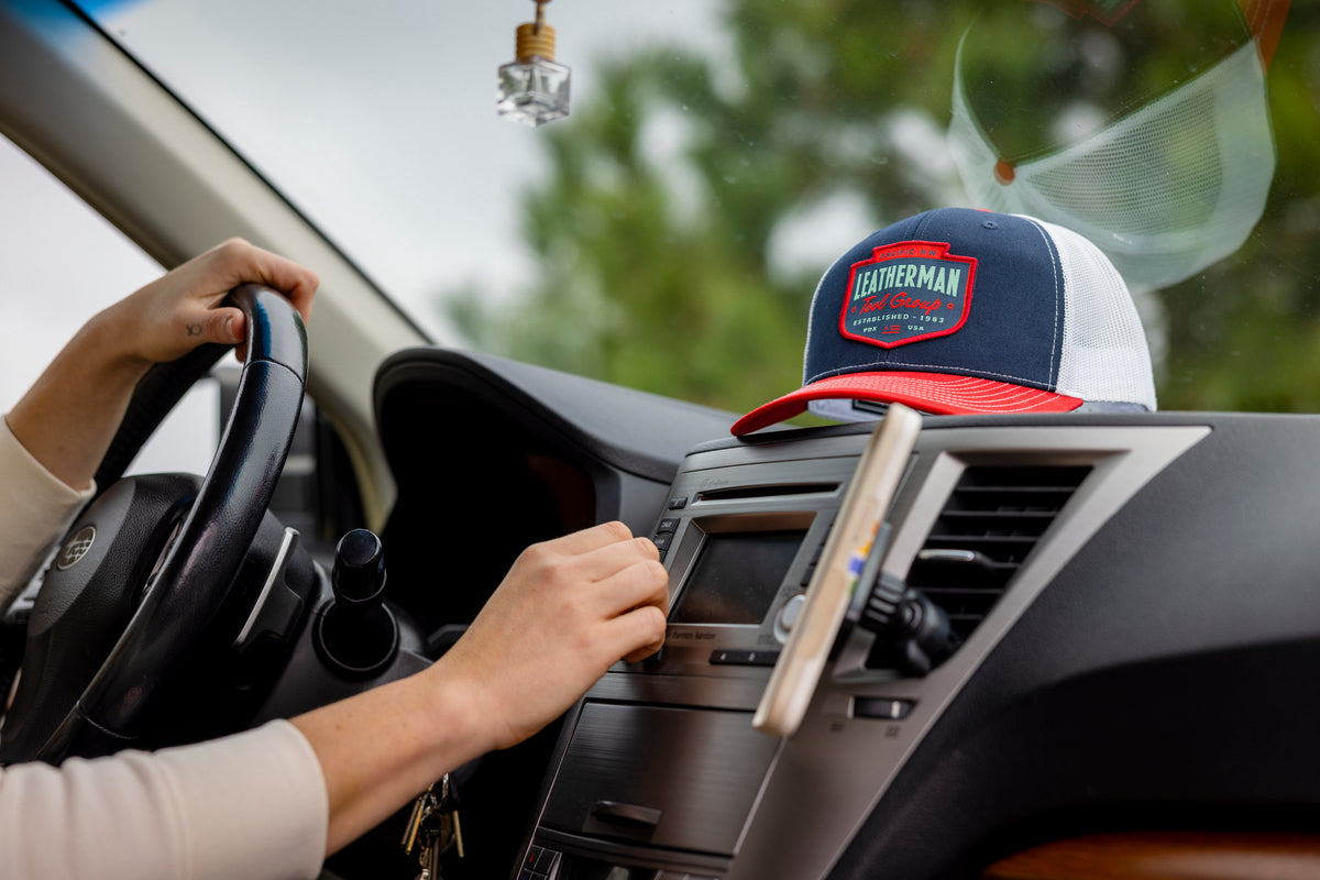 Translation missing: es.A person in a car with a navy Leatherman PNW Trucker Hat with a white mesh back and red brim resting on the dashboard