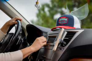 Translation missing: es.A person in a car with a navy Leatherman PNW Trucker Hat with a white mesh back and red brim resting on the dashboard