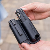 Translation missing: es.Hands holding a black leather sheath carrying two black multitools outdoors