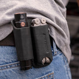 Translation missing: es.Black leather belt sheath holding a multitool and flashlight on a person’s hip