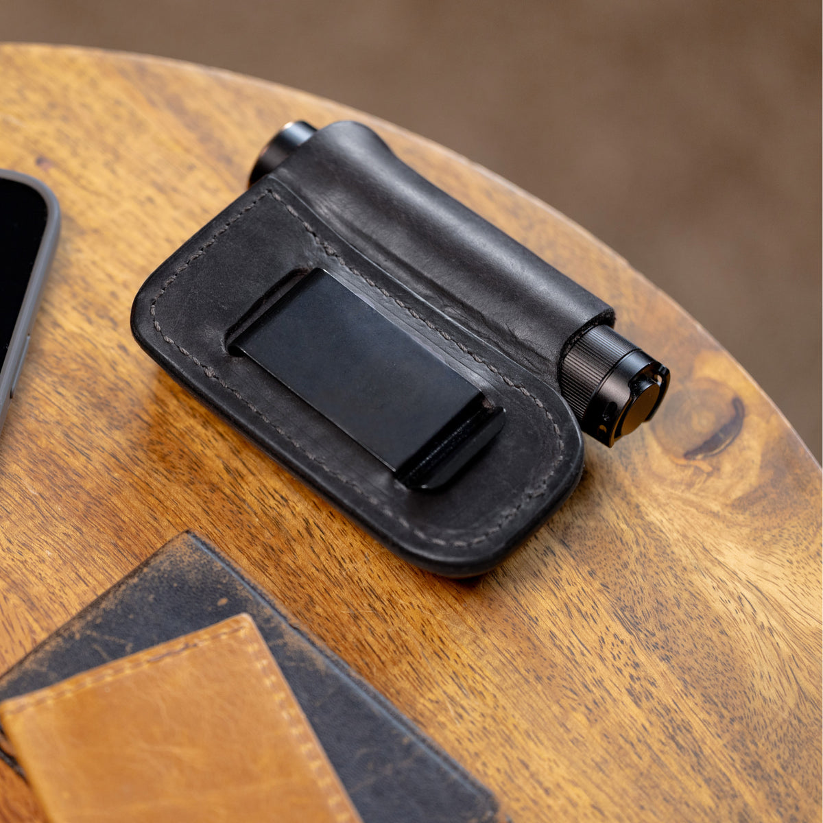 Translation missing: es.Black leather sheath with belt clip holding a small cylindrical flashlight on a wooden surface