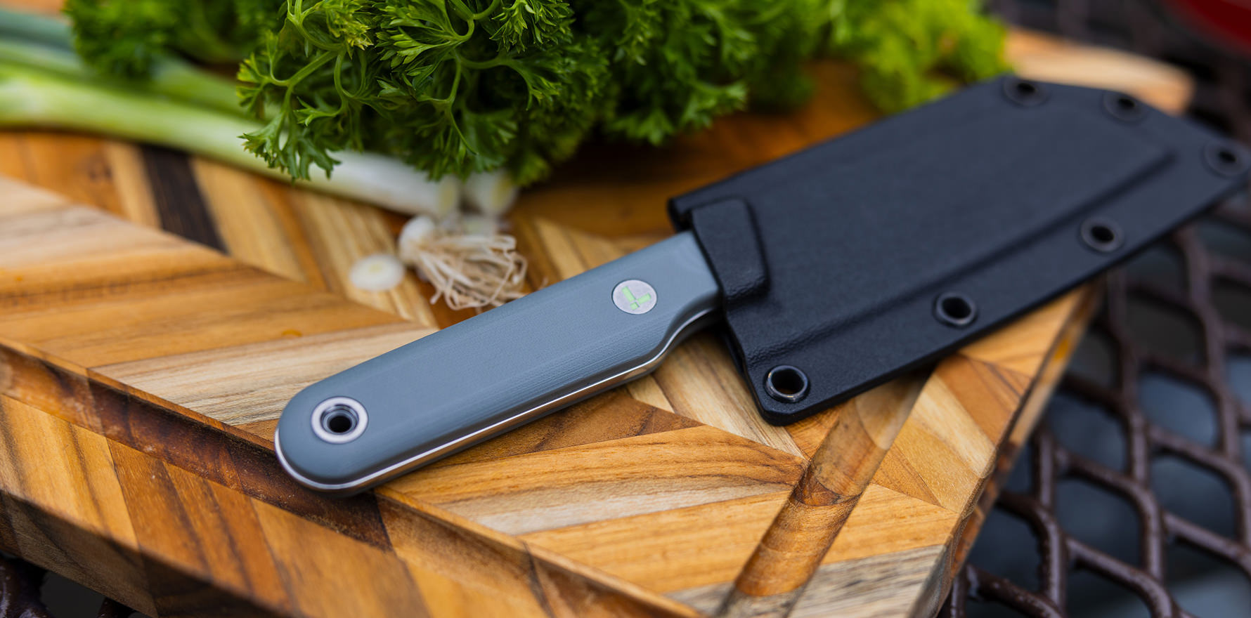 Vapor grey Rustle in kydex sheath on a cutting board next to fresh herbs