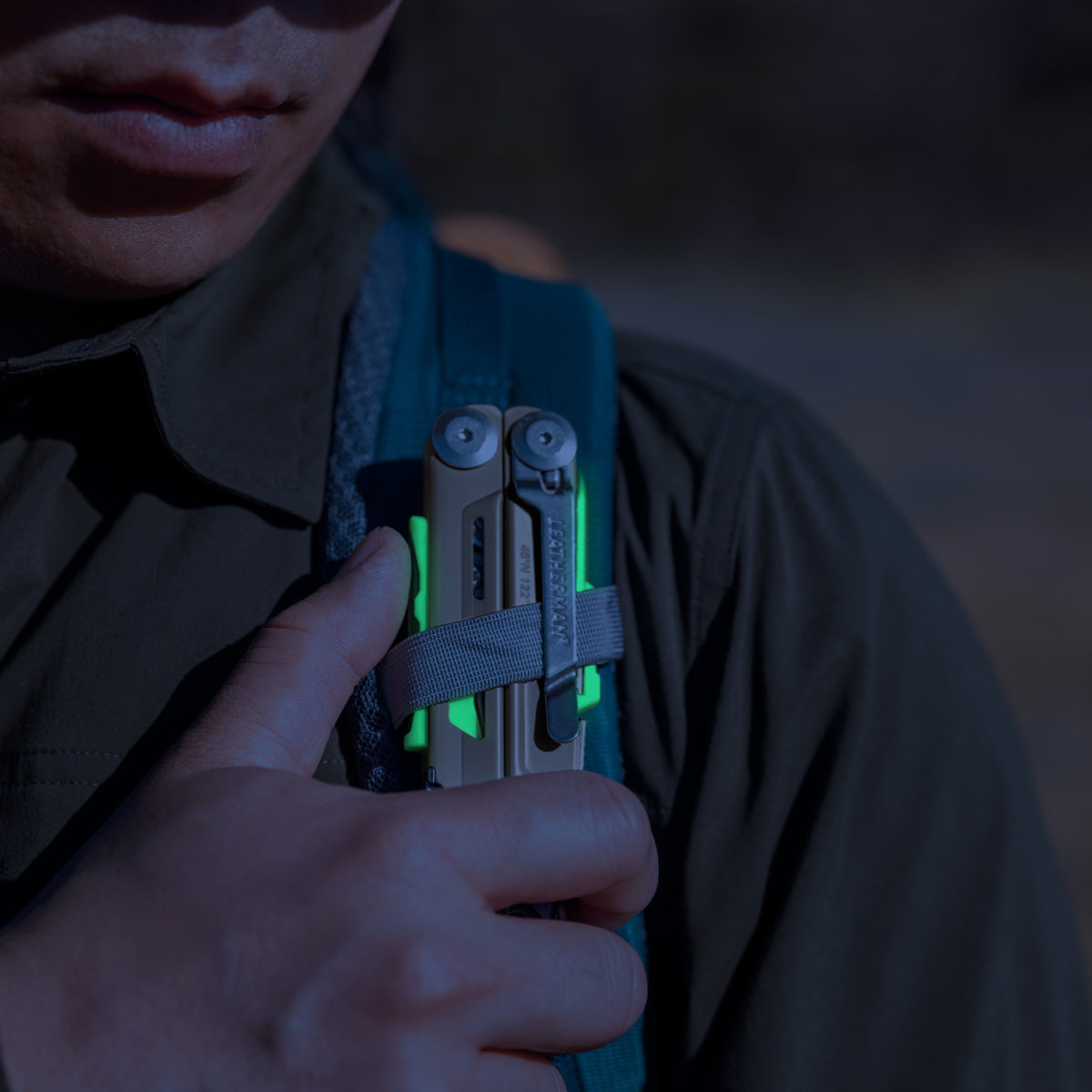 Translation missing: en.Person securing a Signal Sandstorm multitool with neon accents to a backpack strap outdoors