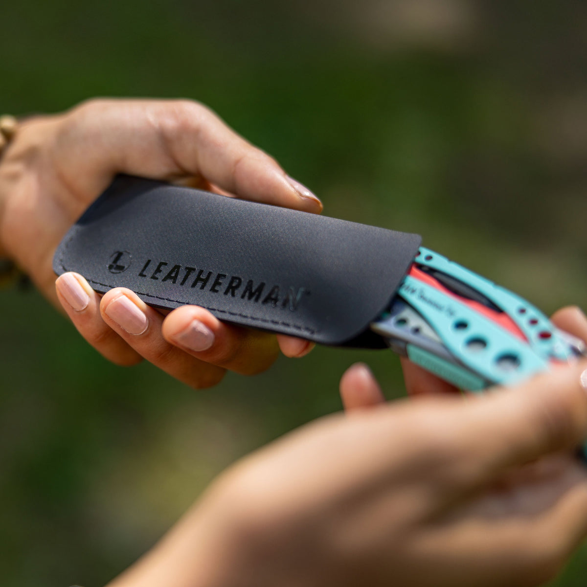 Translation missing: en.A black Leatherman Hypalon tool sleeve held in hand with a partially inserted Paradise-colored Skeletool® CX multi-tool, highlighting the tool’s vibrant design and protective carrying case